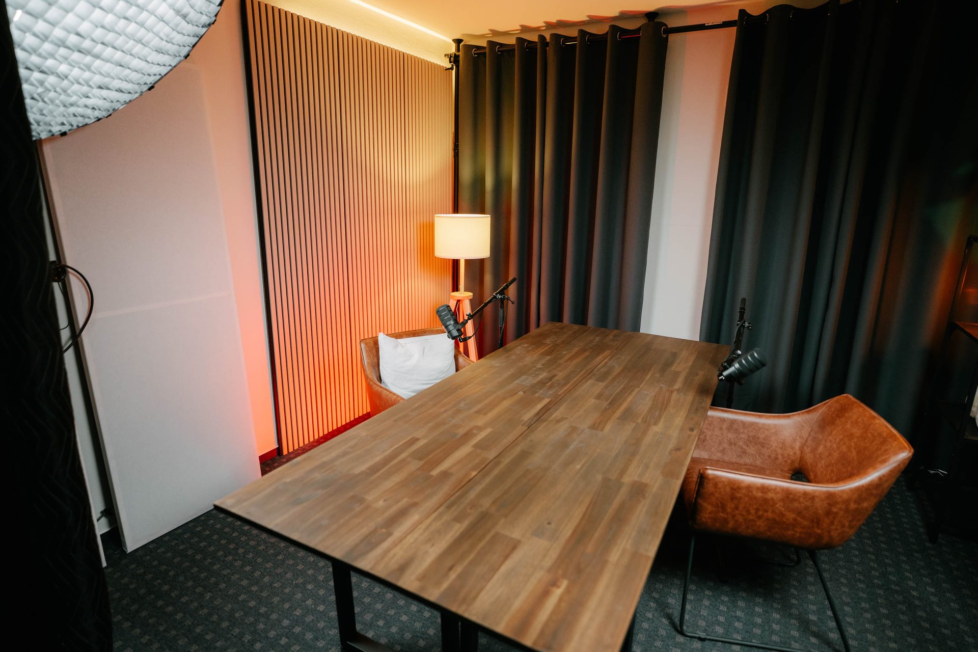 Blick in Studio Eiche – Holztisch mit Ledersesseln, dunkle Vorhänge und warmes Licht